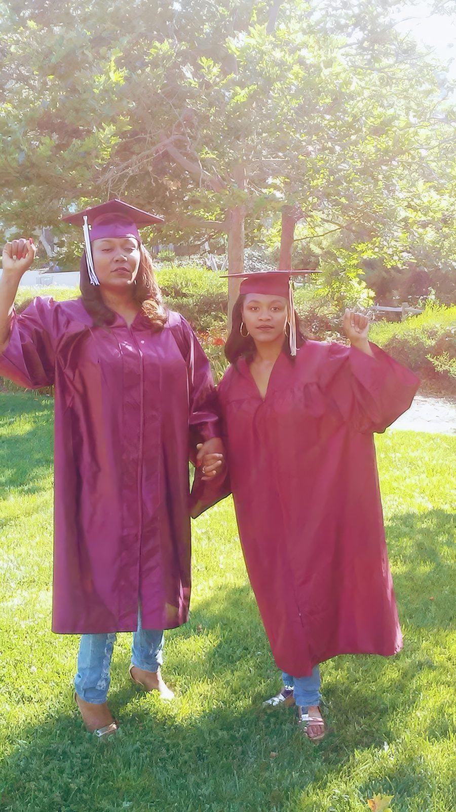 Two graduates in maroon caps and gowns raise their fists outdoors